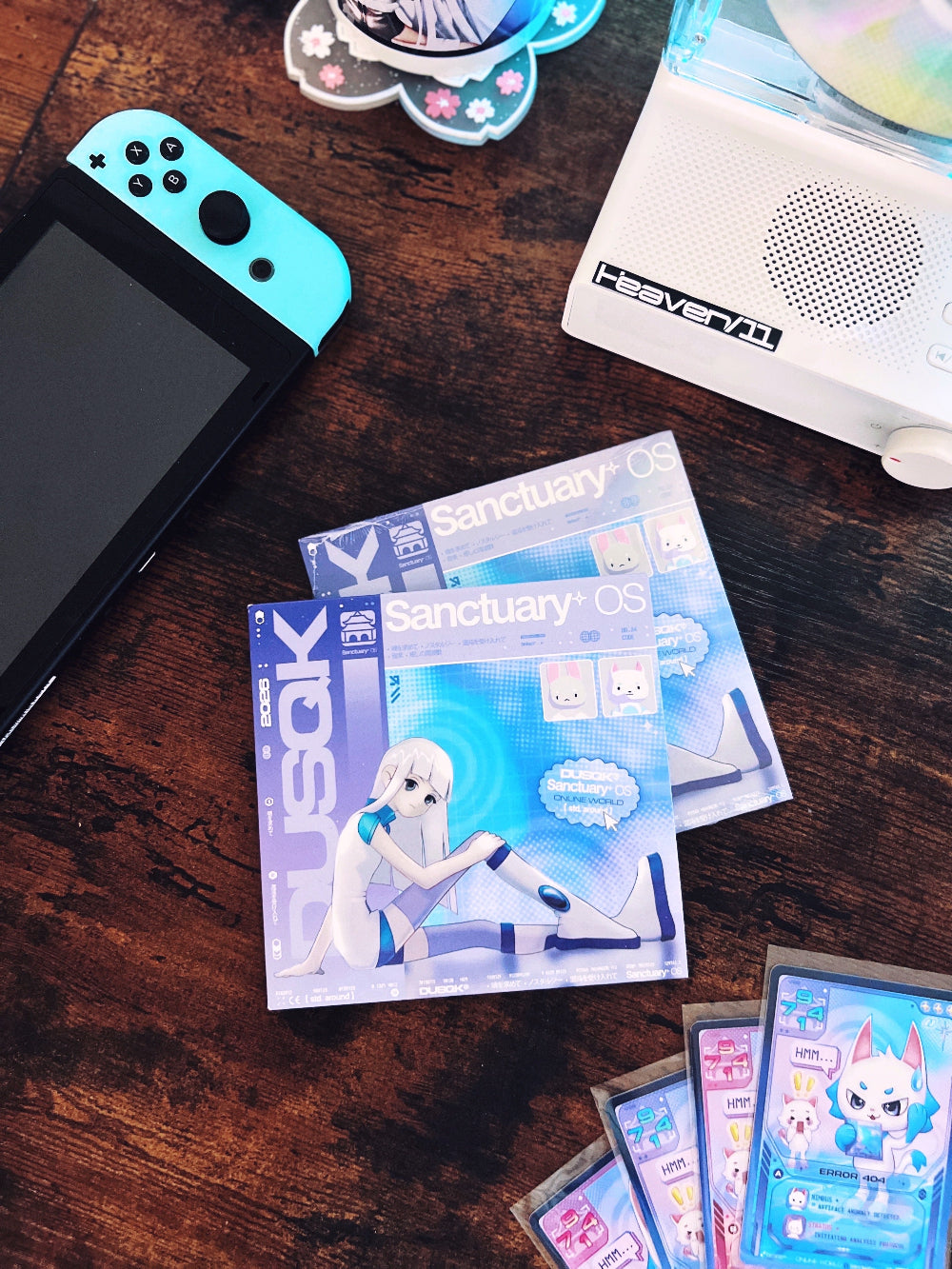 Sanctuary OS CD in cardboard jacket, with CD player, game console, and trading cards in background