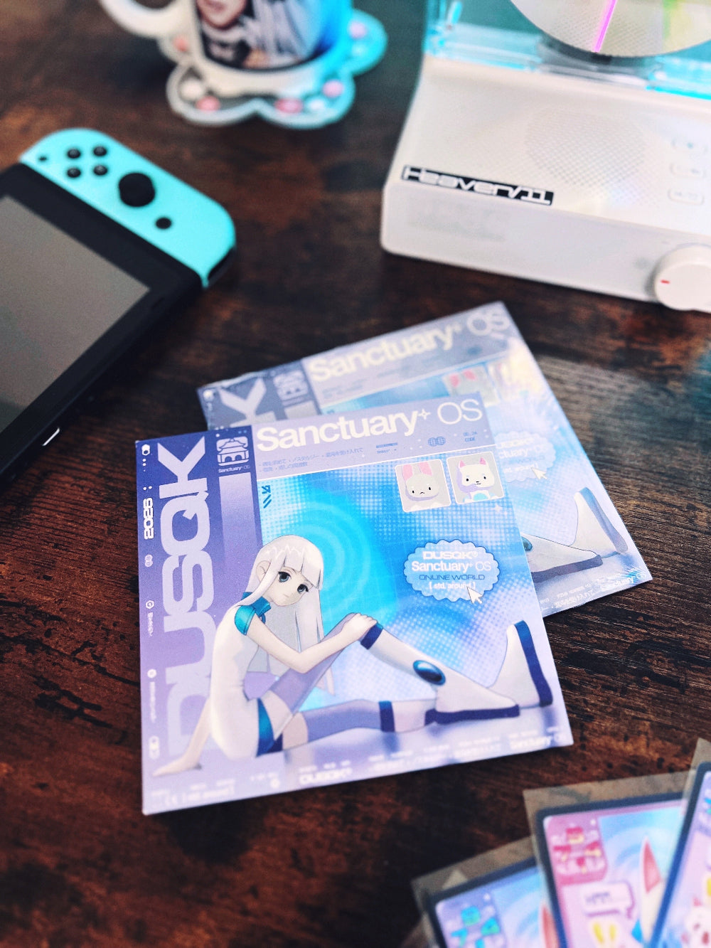 Sanctuary OS CD with cardboard jacket, mug, CD player, game console, and trading cards in background