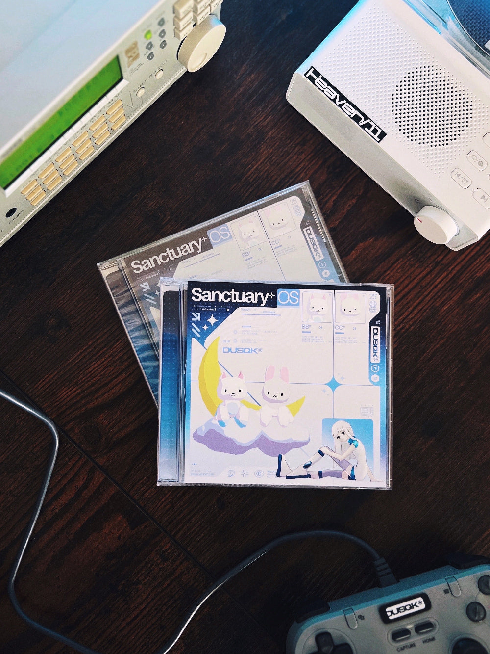 Two Sanctuary OS CDs in jewel case, with CD player, Mu128, and game controller in background